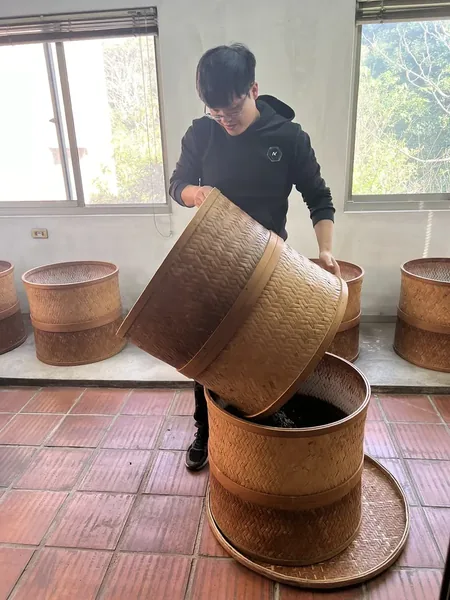在焙茶室裡，把茶葉從一個竹編焙籠倒進另一個
